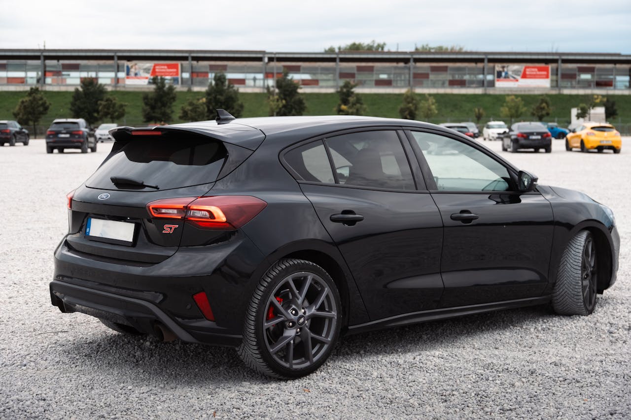 Modern black hatchback car parked in a spacious outdoor lot with other vehicles in view.